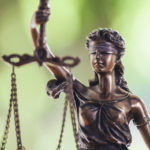 Close up photograph of a Lady of Justice statue with a green background.