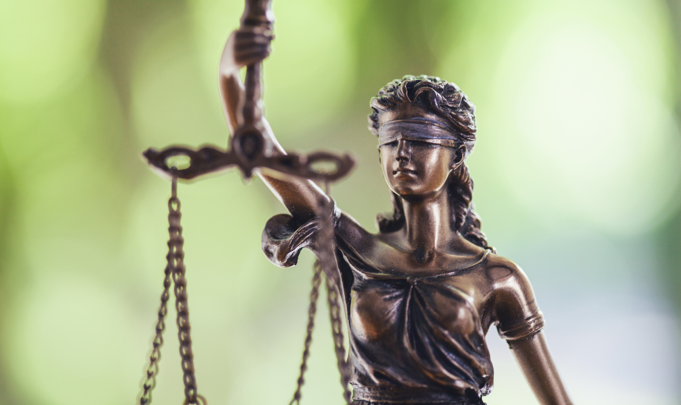 Close up photograph of a Lady of Justice statue with a green background.