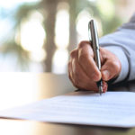 Close up photograph of a person signing a document in an office setting.
