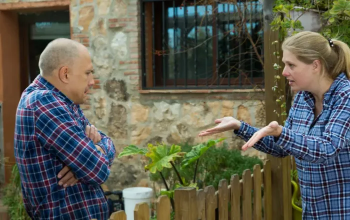 Two neighbors arguing across a property fence, representing a property encroachment dispute involving boundaries and neighboring land.