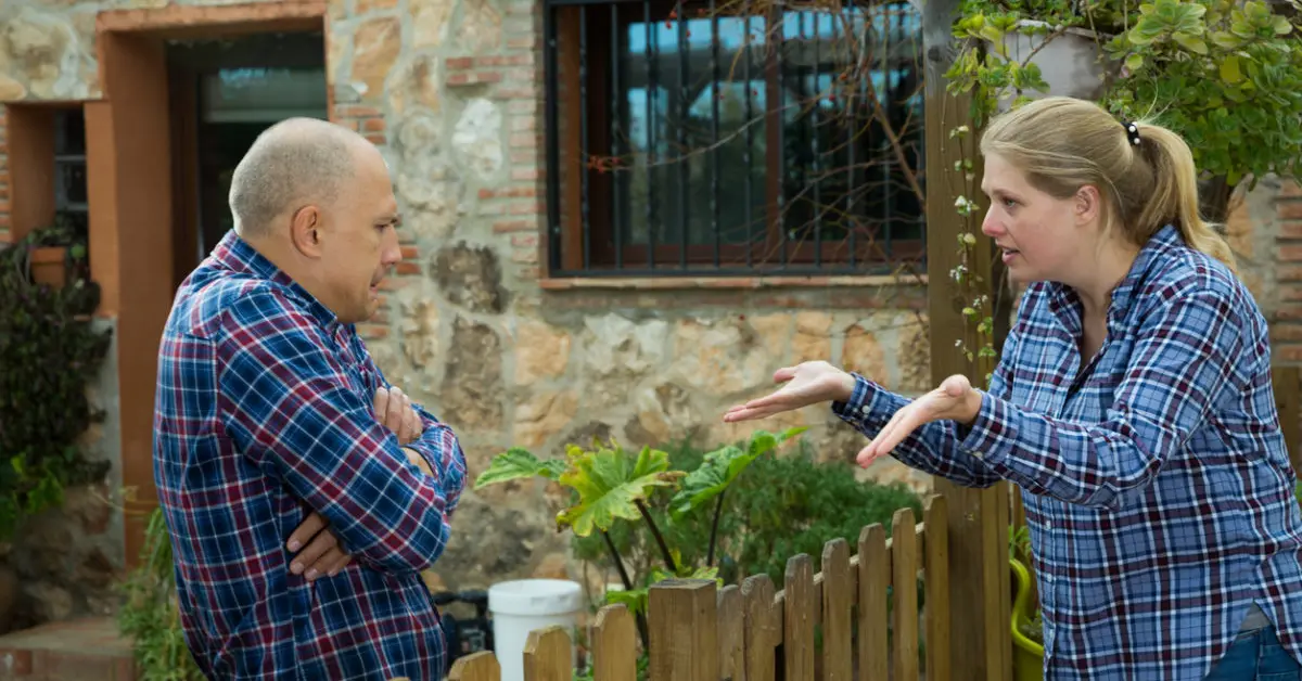 Two neighbors arguing across a property fence, representing a property encroachment dispute involving boundaries and neighboring land.