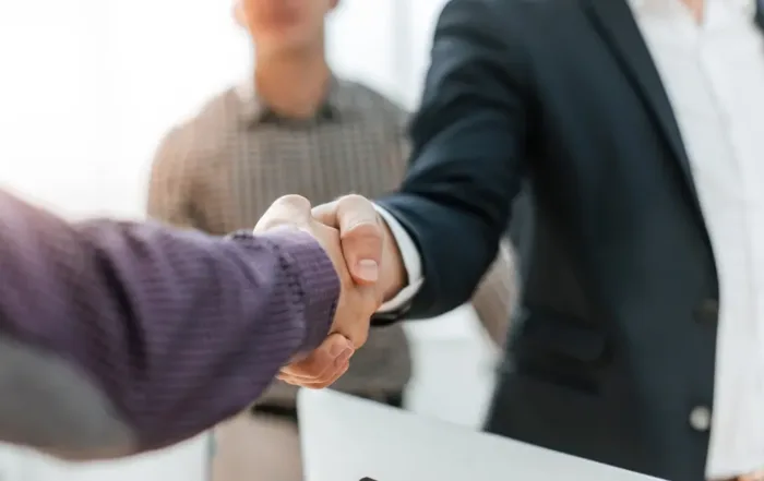 Two business professionals shaking hands in an office setting, symbolizing a general partnership or business agreement.