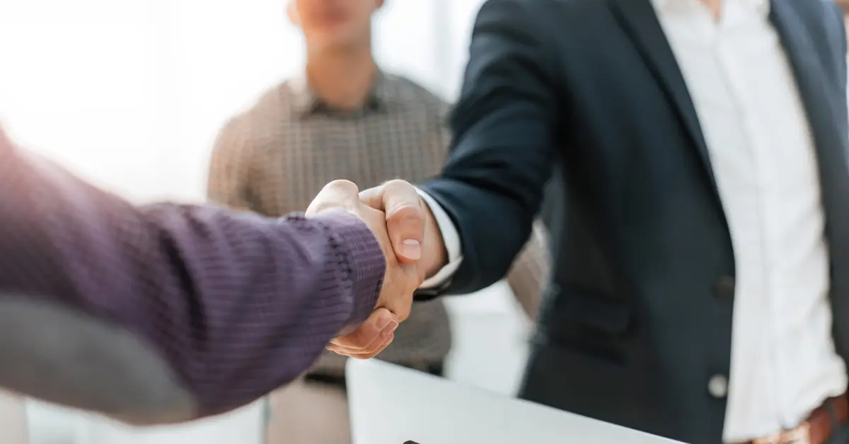Two business professionals shaking hands in an office setting, symbolizing a general partnership or business agreement.