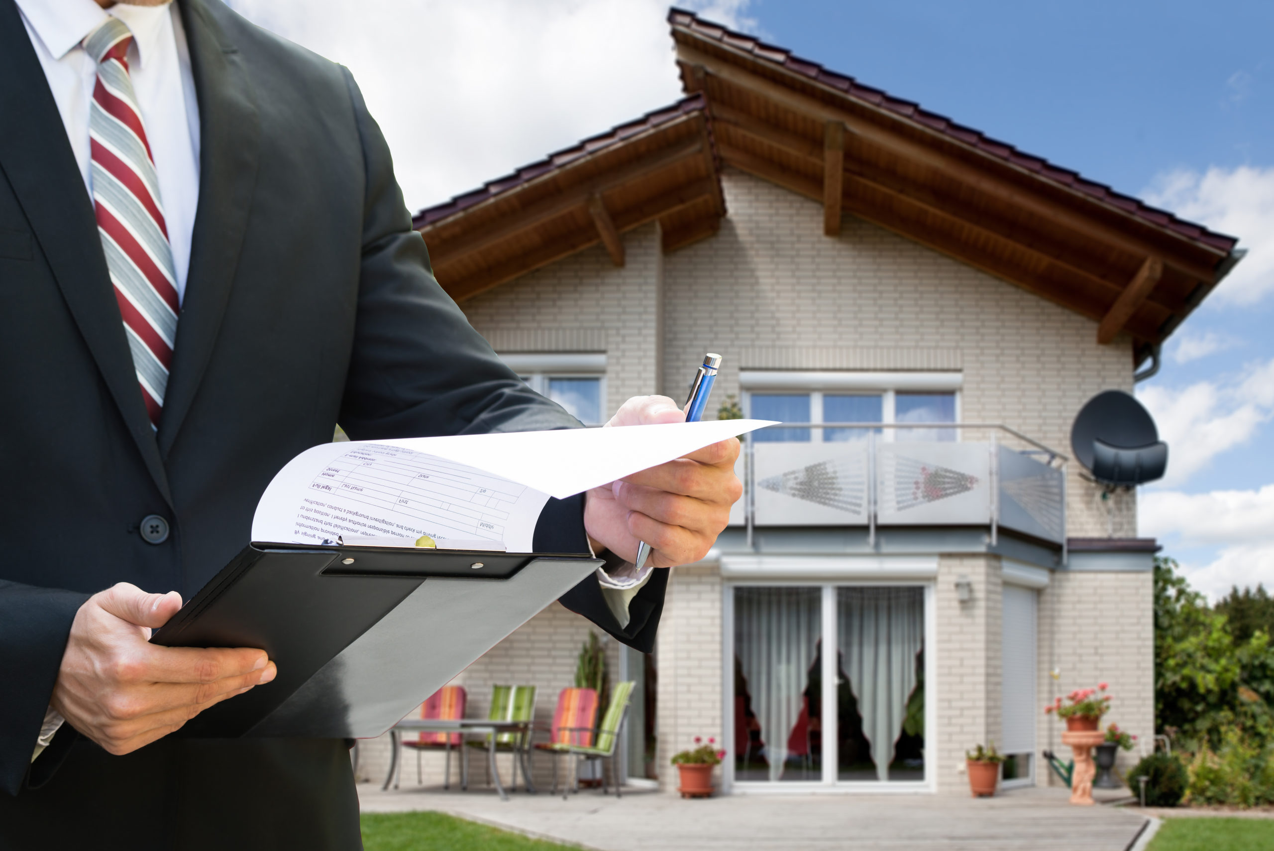 Man in suit looking at papers while standing in front of a house