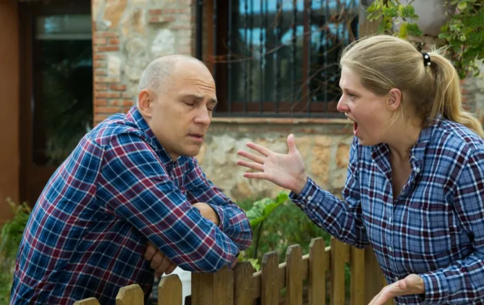 Frustrated woman yelling at her neighbor during a heated argument over a fence, highlighting neighbor disputes and property conflicts