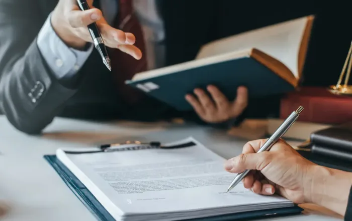 A litigator discussing legal documents with a client at a desk, holding a pen and law book