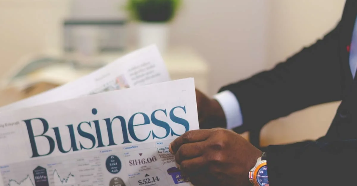 Close-up of a person in a suit holding a newspaper with the headline “Business,” symbolizing financial news, market updates, and corporate insights.